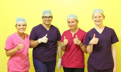 Students in scrubs and caps showing thumbs up